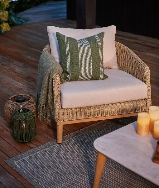 Outdoor lounge chair with cushions and a throw beside a lantern